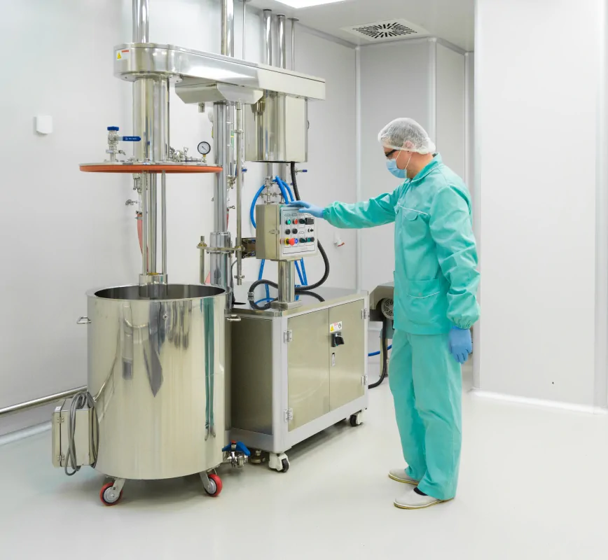 Pracownik w kombinezonie obsługuje maszynę w komorze farmaceutycznej.